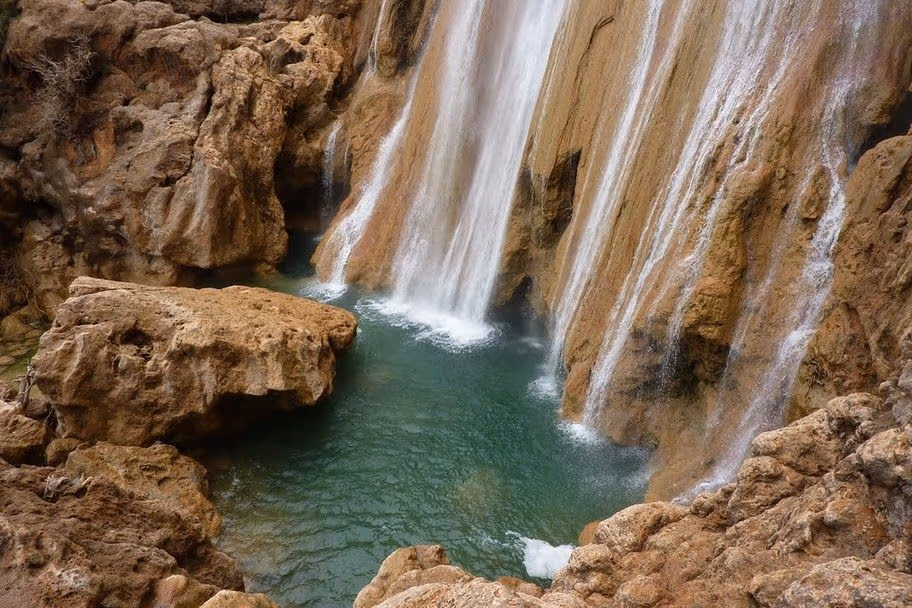 The Imouzzer waterfall cascading over travertine cliffs into a green pool